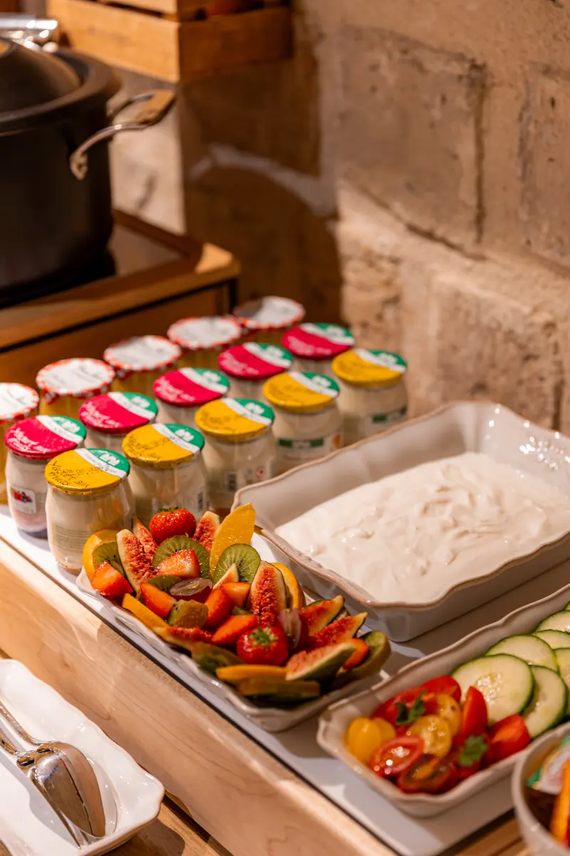 Buffet frais : yaourts en pots colores, plateau de fruits frais (fraises, kiwi, figues), fromage blanc et crudites