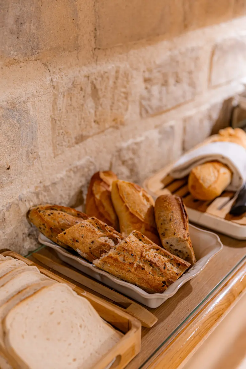 Corbeilles de pains varies : baguettes aux graines, pain de mie et petits pains sur etagere bois, mur en pierre