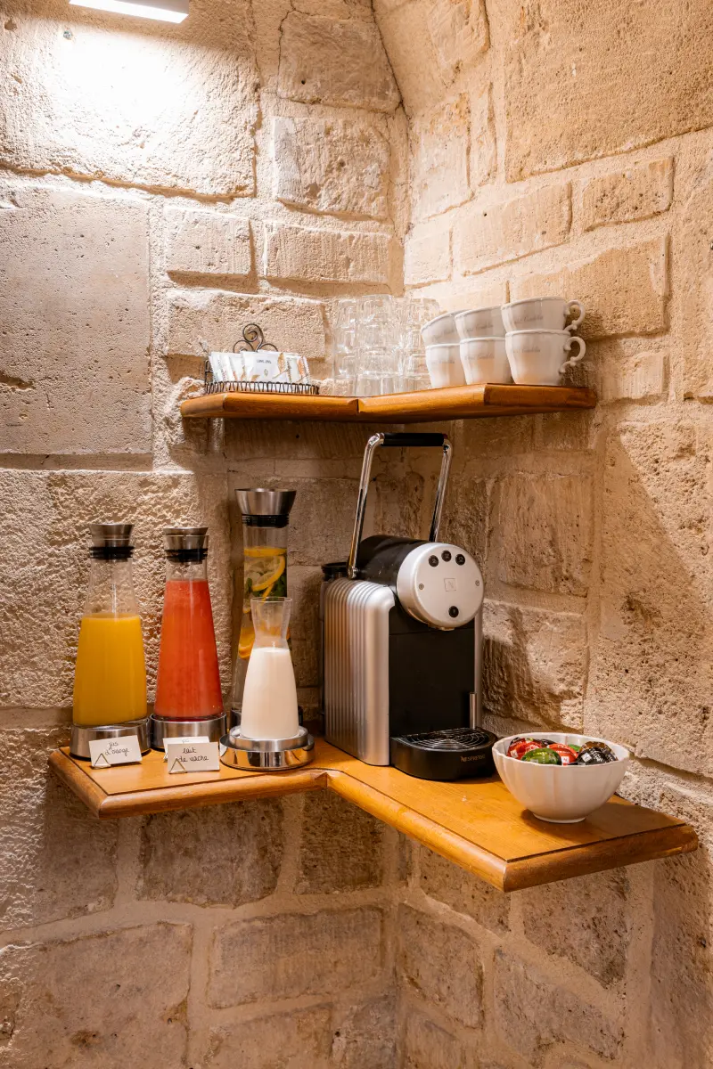Angle de salle en pierre avec carafes de jus de fruits, machine a cafe Nespresso et tasses empilees