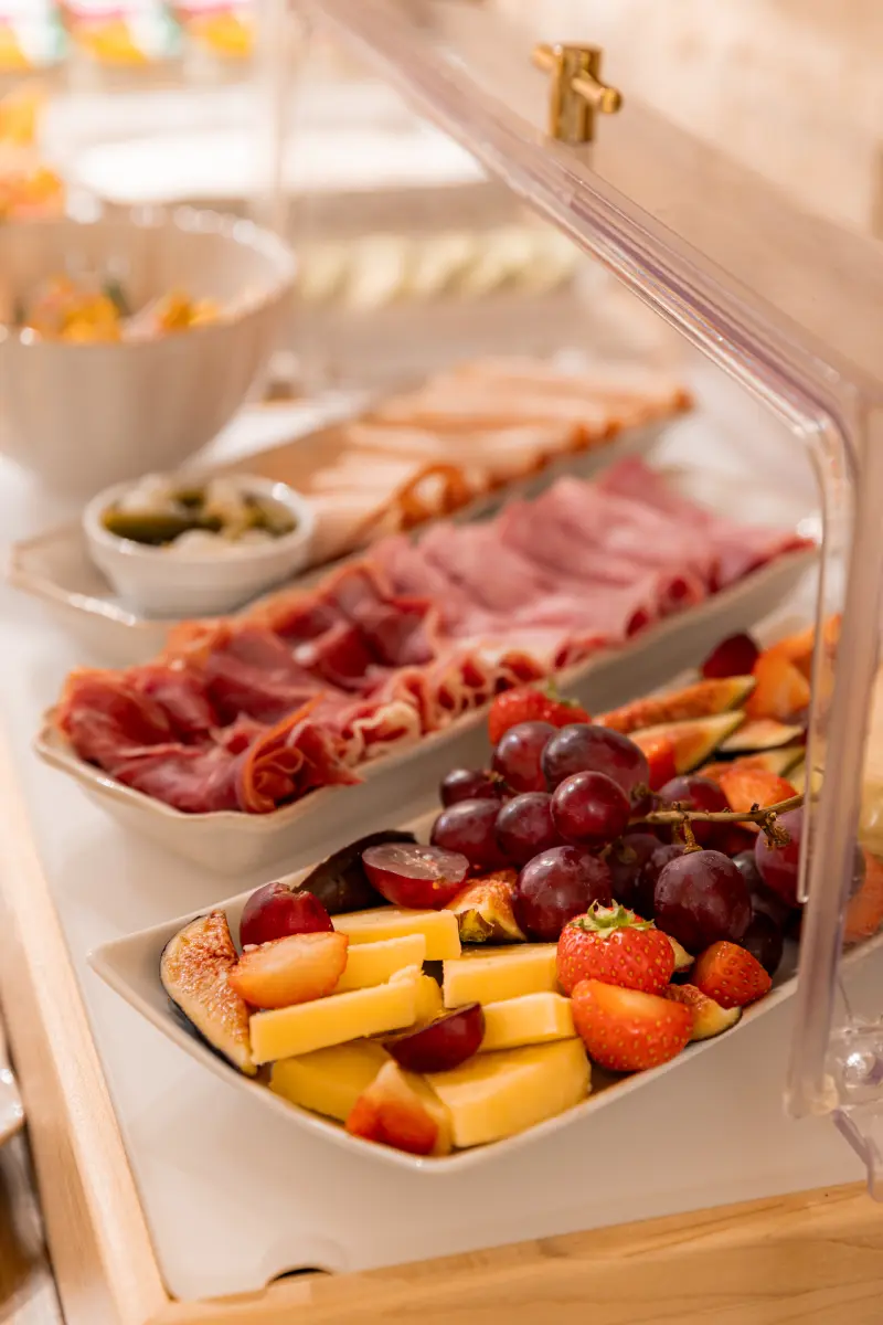 Buffet refrigere avec plateaux de charcuteries, fromages tranches et fruits frais (raisins, fraises, figues)